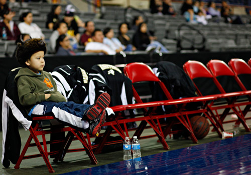 Cecil, the son of Sonny Eppinette, a Salish Kootenai College basketball student athlete, enjoys the games from the bench donning a buffalo hat while his father is playing.