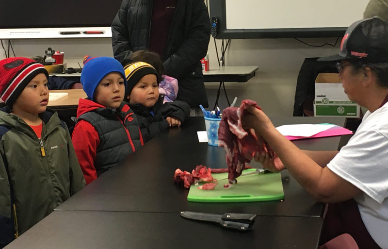 Children learning how meat is thinly sliced in preparation for drying.